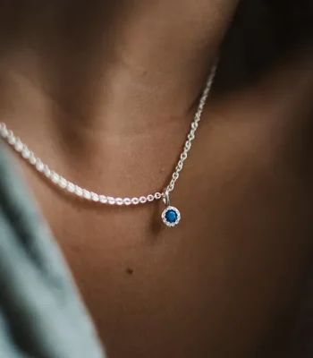 Close up of models neck wearing a silver chain with a sapphire birthstone pendant.