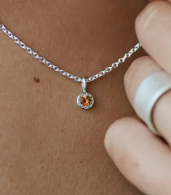 Close up of a silver chain with a yellow topaz birthstone pendant attached.